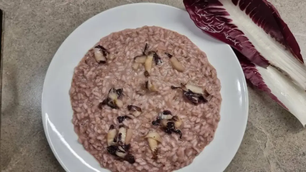 Un cremoso risotto al radicchio, con pezzetti di verdura che spuntano, accanto a una foglia fresca di radicchio.