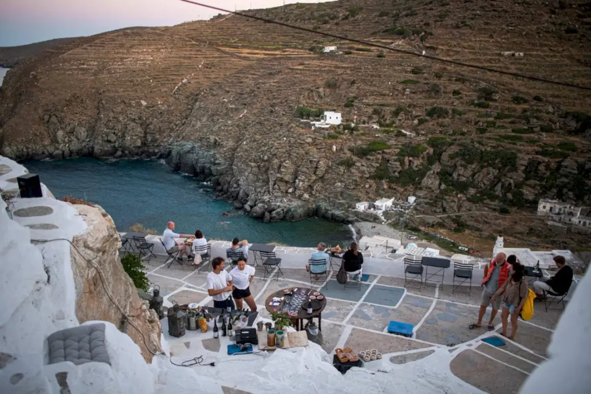 Människor njuter av en måltid på en terrass med utsikt över en vik på Sifnos, Grekland.