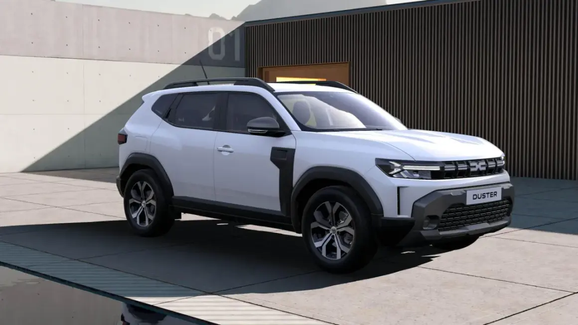 Nowa Dacia Duster w białym kolorze prezentuje się nowocześnie na tle betonowej ściany i budynku z drewnianymi elementami.