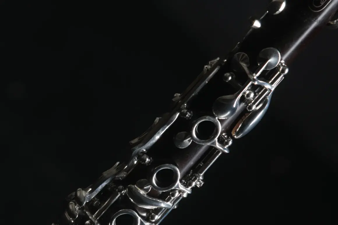 Nahaufnahme eines dunklen Holzblasinstruments, einer Klarinette, mit glänzenden Metallklappen vor schwarzem Hintergrund.
