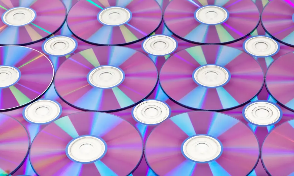 Stos płyt CD/DVD z fioletowo-niebieskimi refleksami, widoczne środkowe otwory.