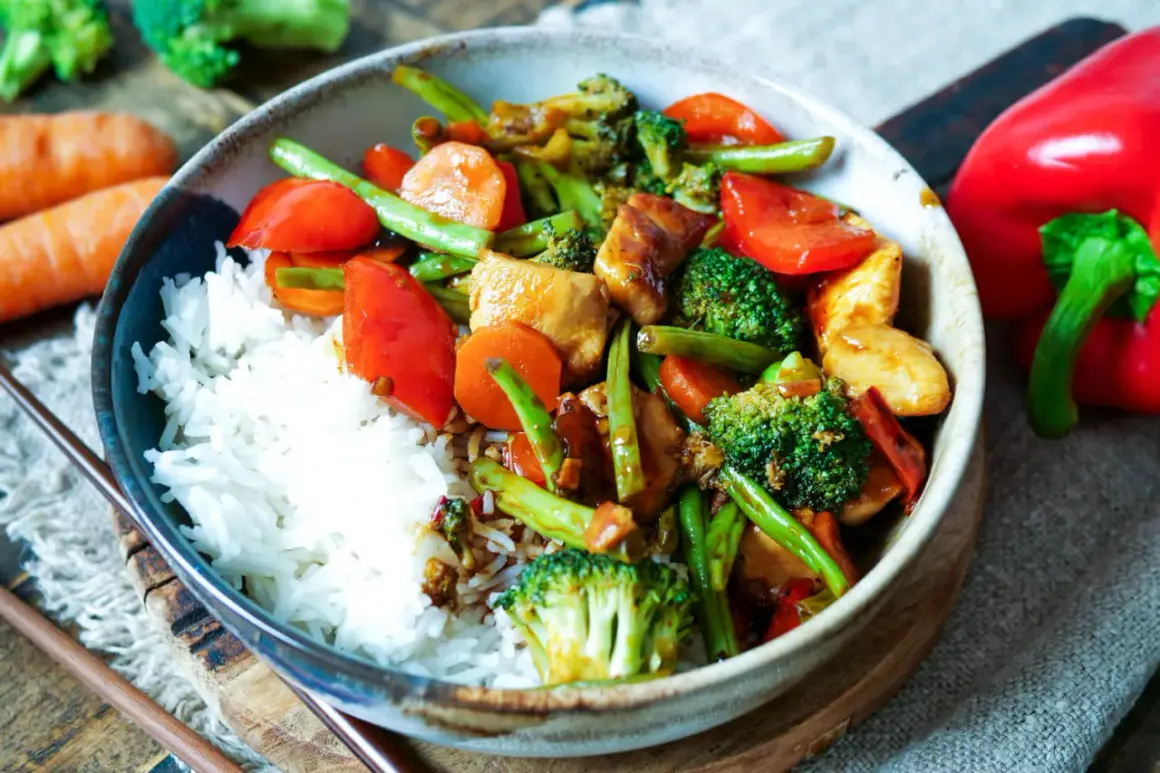 Schüssel mit Reis und buntem Chop Suey: Hühnchen, Brokkoli, Karotten, Paprika und grüne Bohnen in einer herzhaften Sauce.