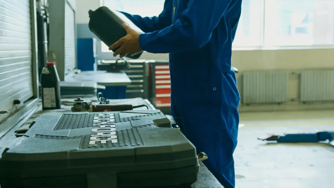 Meccanico in tuta blu prepara il cambio olio motore fuoribordo 4 tempi, tenendo una tanica di olio.