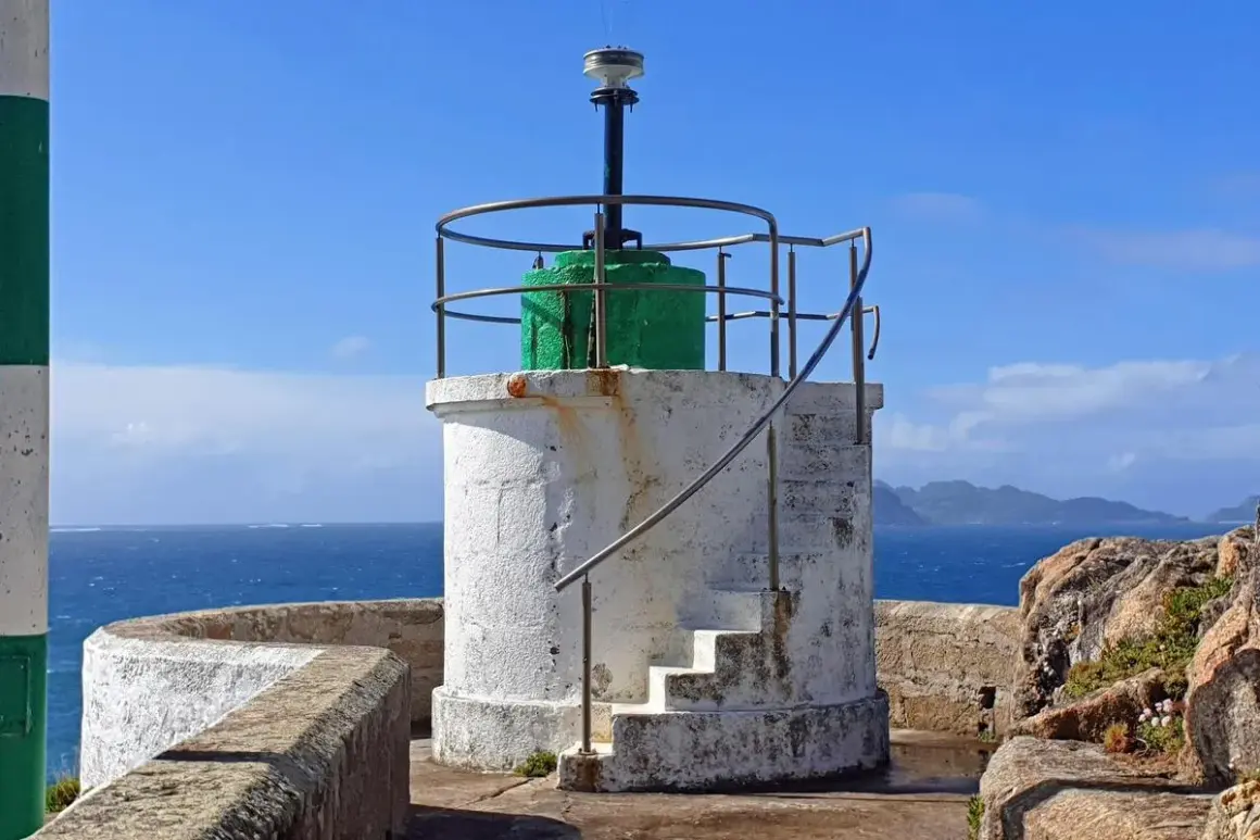 Faro blanco con base verde y escaleras externas, junto al mar azul. El **monte Ferro** se divisa al fondo.