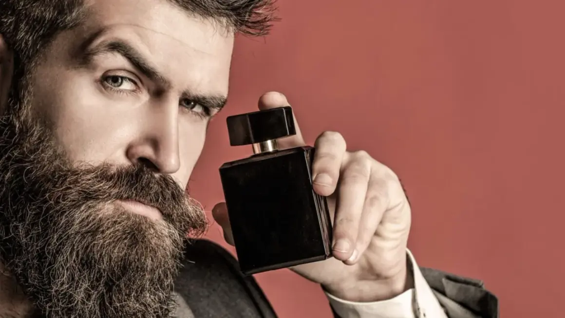 Mężczyzna z brodą trzyma czarną buteleczkę perfum, zastanawiając się, gdzie psikać perfumy, by podkreślić swój styl.