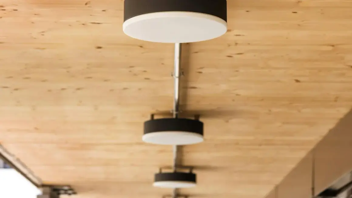 Nowoczesne lampy, każdy plafon ścienny z czarną obudową i białym dyfuzorem, zamontowane na drewnianym suficie.