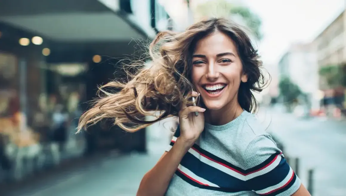Lachende Frau telefoniert, ihr Haar weht im Wind. Sie genießt ihr **iu auslandssemester** in der Stadt.