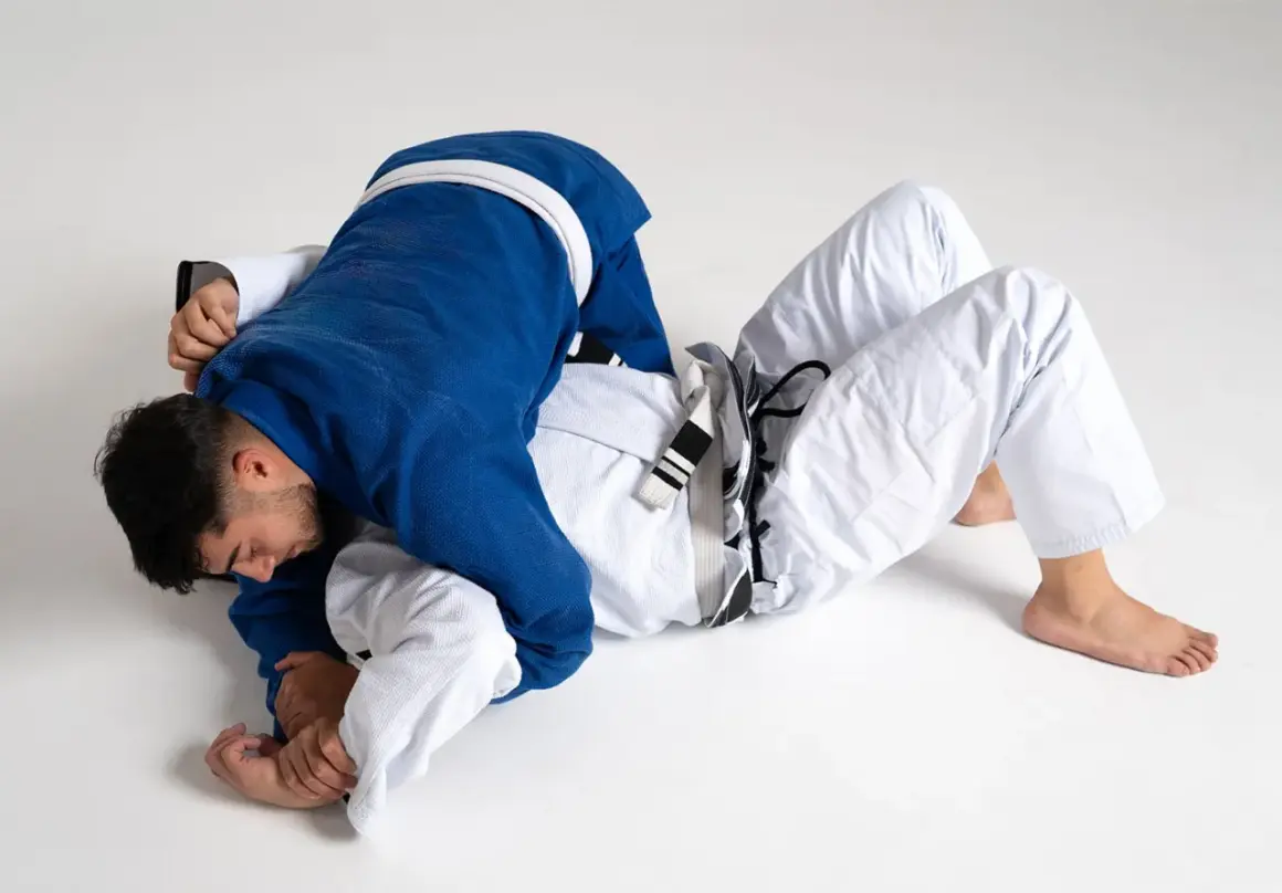 Två män i judodräkter brottas på golvet. En blå och en vit dräkt, en kamp mellan judo vs bjj.