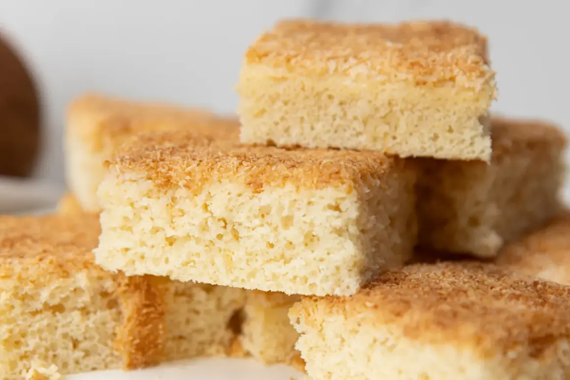 Stapel von saftigen Buttermilch Kokos Kuchenstücken, goldbraun gebacken und mit Kokosraspeln bestreut.