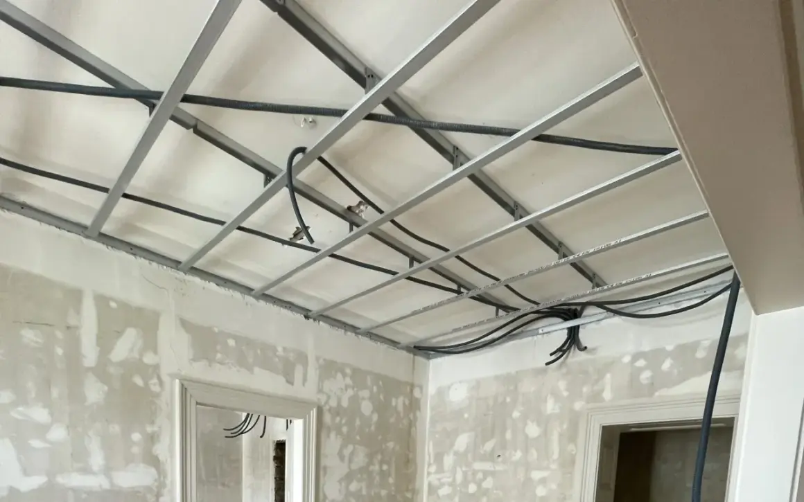 Structure métallique pour faire un faux plafond, avec des câbles électriques en cours d'installation. Les murs sont en chantier.