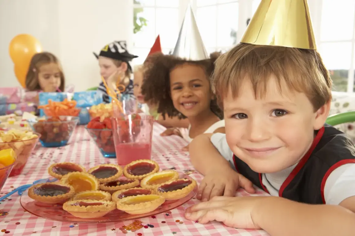 Glada barn med kalashattar vid ett dukat bord med tårtor och frukter. Perfekt för kalaslekar 5 år!