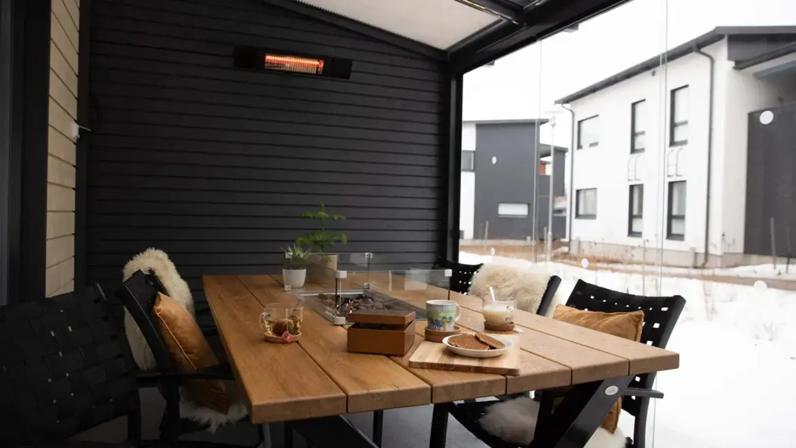 Mesa de madera en terraza cerrada con calefactor, ideal para disfrutar de una bebida caliente en invierno.