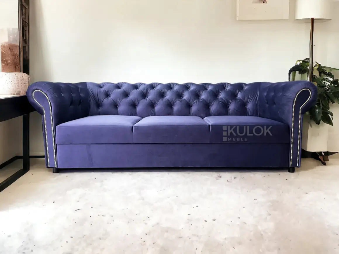 Elegancka, granatowa kanapa chesterfield z pikowanego welwetu, ozdobiona srebrnymi pineskami.
