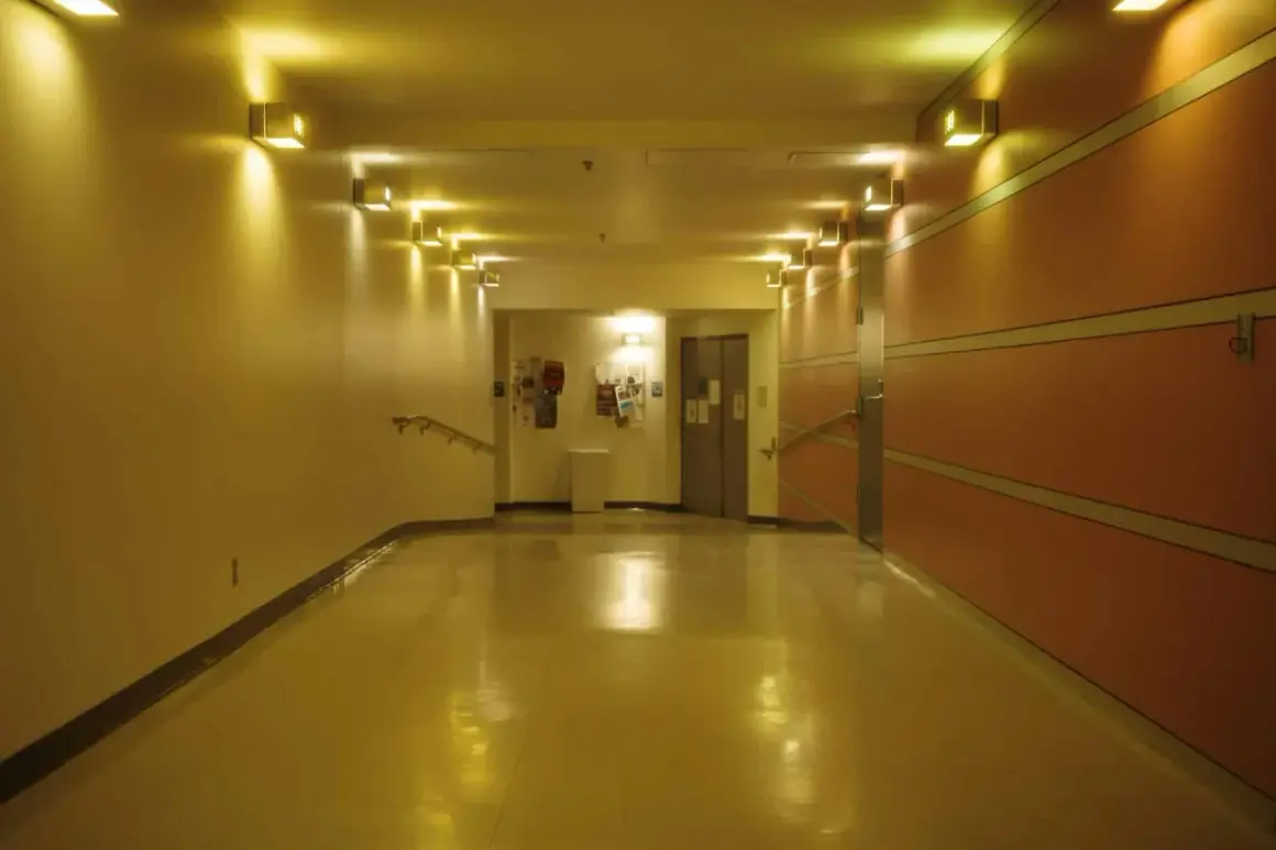 Korytarz z żółtym, błyszczącym podłogą i rzędem lamp. Oświetlenie awaryjne zapewnia bezpieczeństwo.