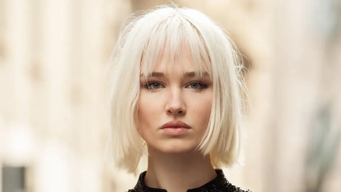 Mujer joven con un moderno corte bob rubio platino y maquillaje sutil.