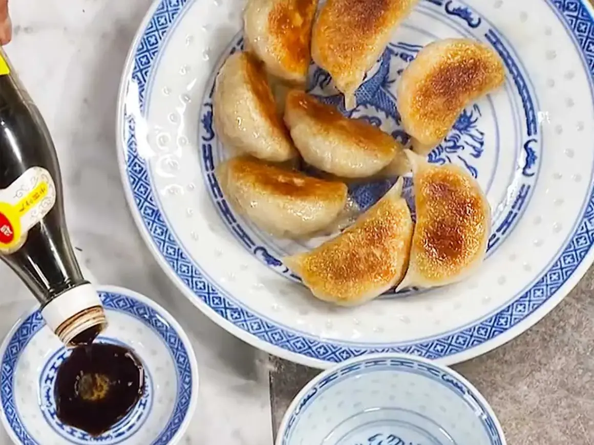 Stekta vegetariska dumplings serveras på en blåvit tallrik. Sojasås hälls upp i en liten skål. Ett perfekt vegetariska dumplings recept!