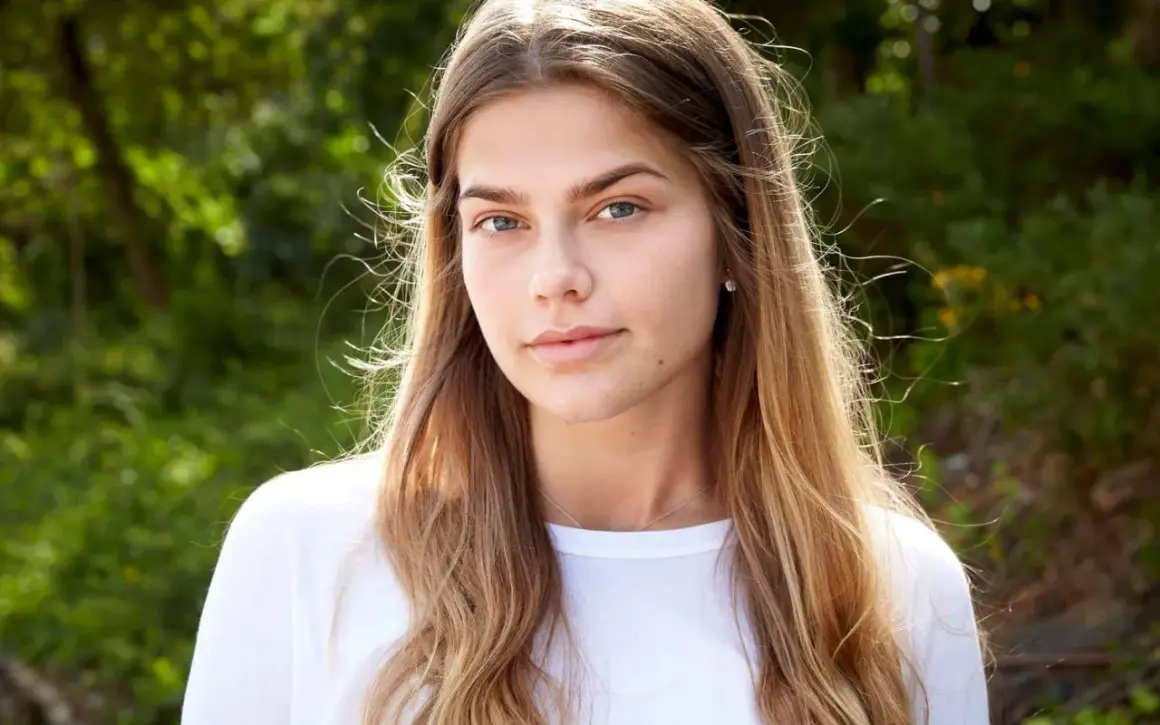 En ung kvinna med blont hår och blå ögon, en blivande top model Sverige, ler mot kameran utomhus.
