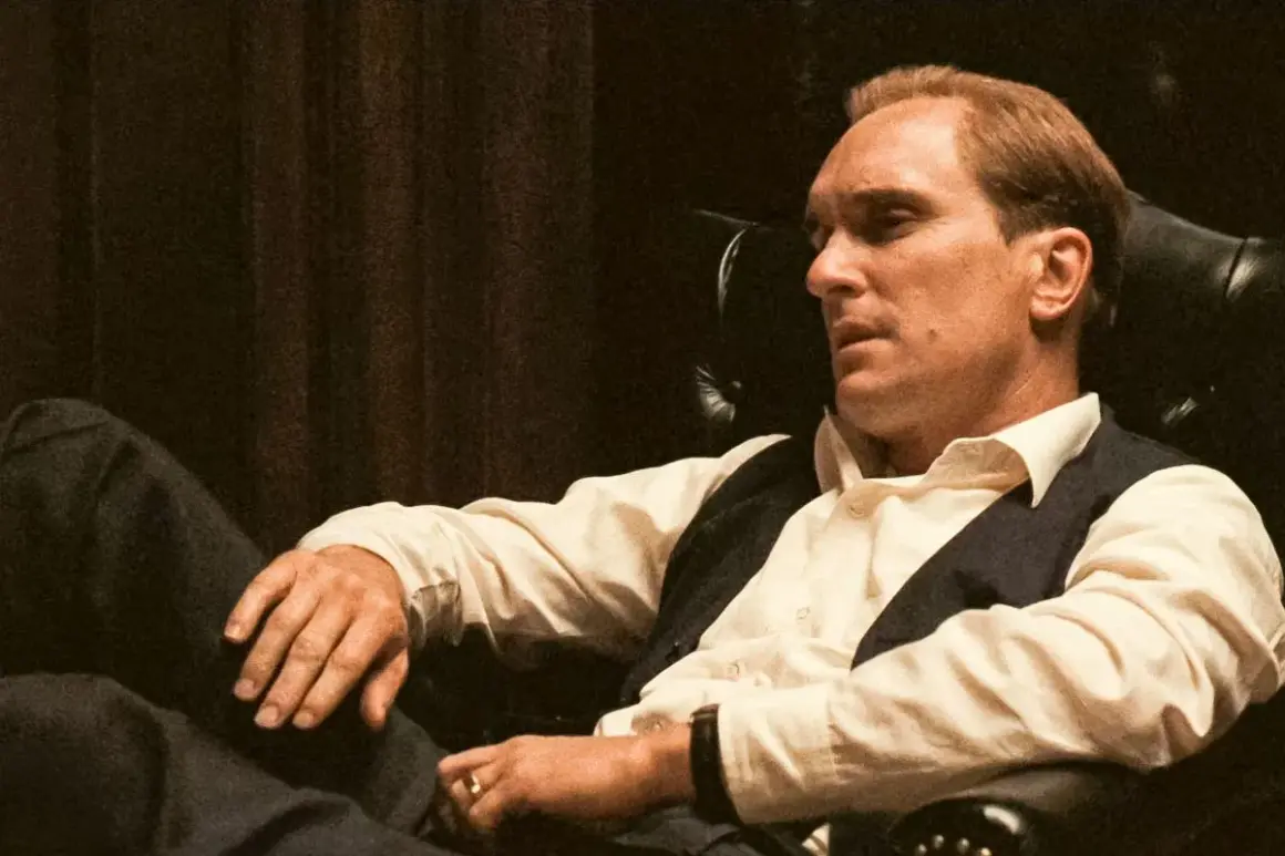 Robert Duvall jako Tom Hagen w fotelu, zamyślony, w białej koszuli i kamizelce.