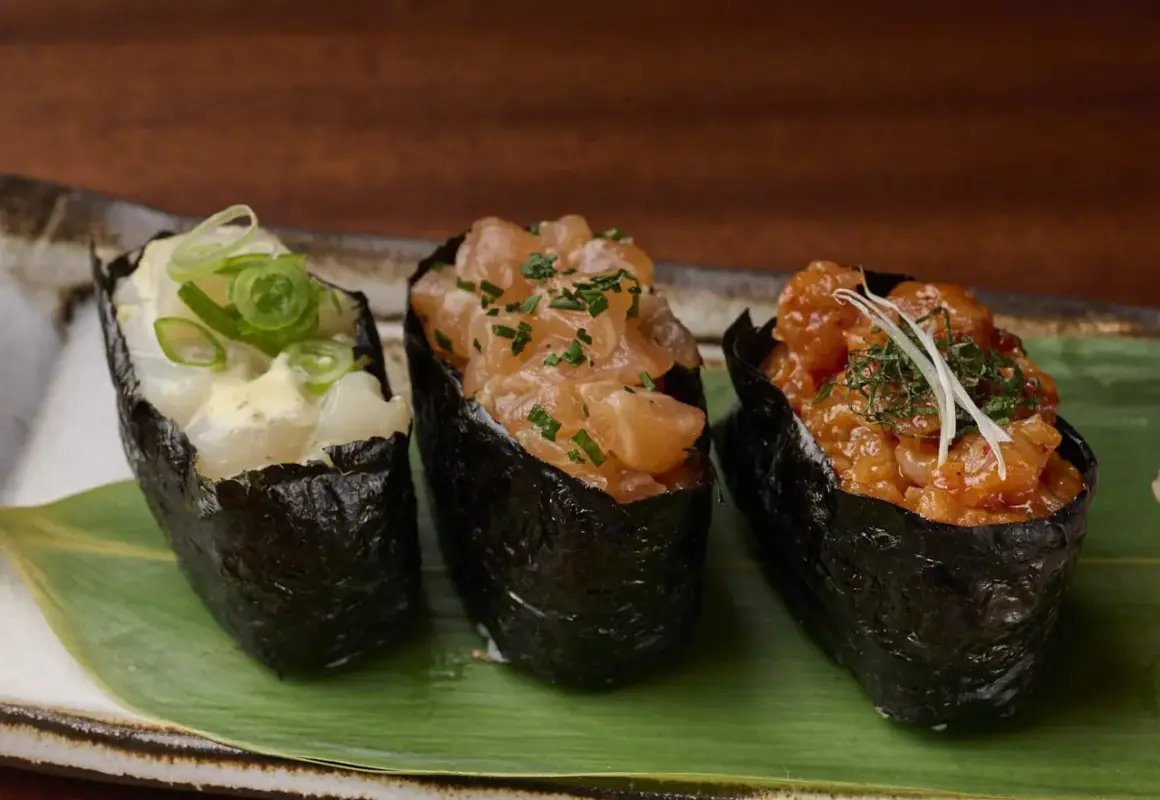 Drei Gunkan-Maki-Sushi mit Lachs, Garnelen und Fisch, garniert mit Frühlingszwiebeln und Kräutern.