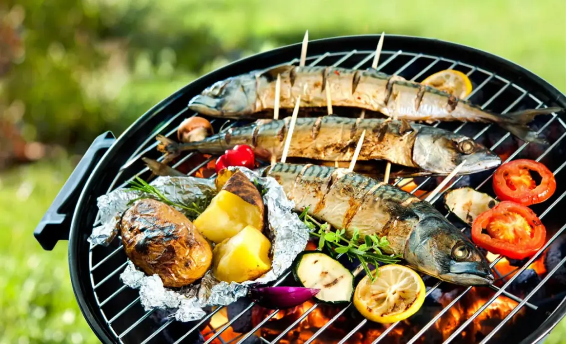 Drei ganze Makrelen werden auf einem Grill mit Kartoffeln, Tomaten und Zucchini gegrillt.