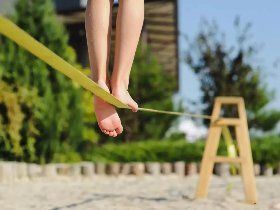 Füße balancieren auf einer gelben Slackline, die an einem Holzgestell befestigt ist.