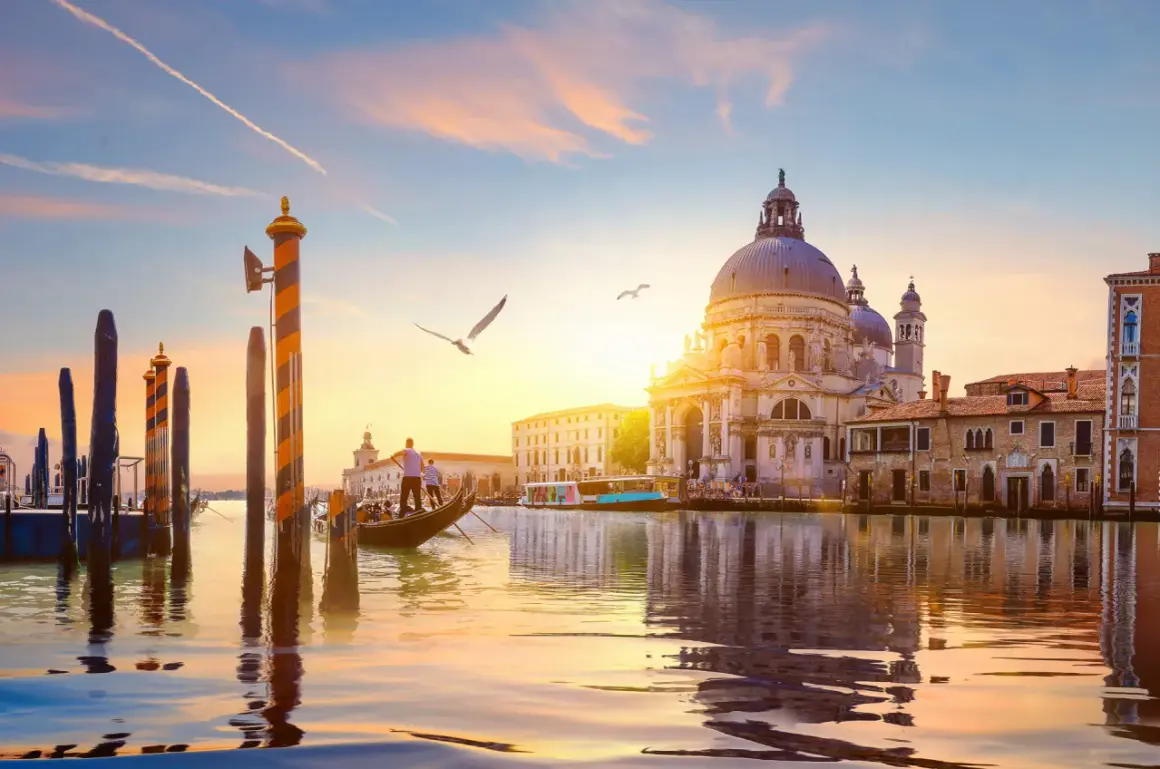 Gondola naviga sul Canal Grande al tramonto, con la maestosa Basilica di Santa Maria della Salute che domina lo skyline.