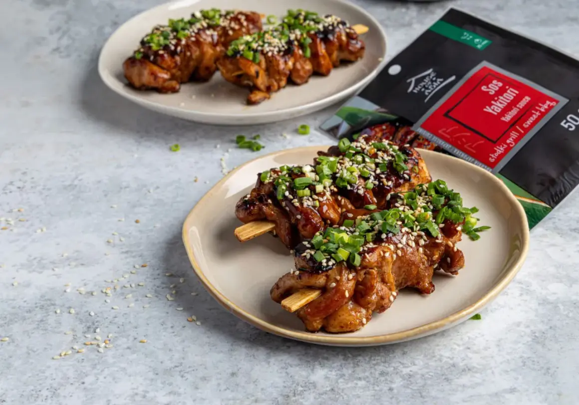 Pyszne yakitori na patyczkach, polane sosem i posypane sezamem i szczypiorkiem. Obok opakowanie sosu Yakitori.