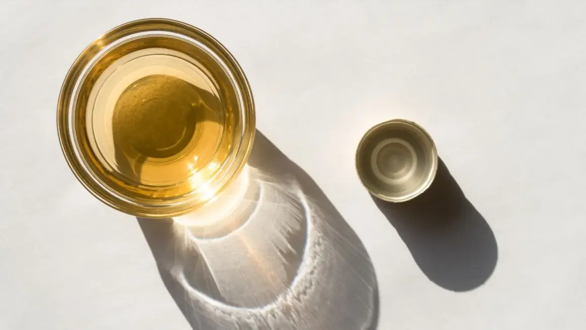 Ein Glas mit goldenem Apfelessig steht neben seinem Deckel. Sonnenschein wirft interessante Schatten. Bereit, Apfelessig zu trinken.