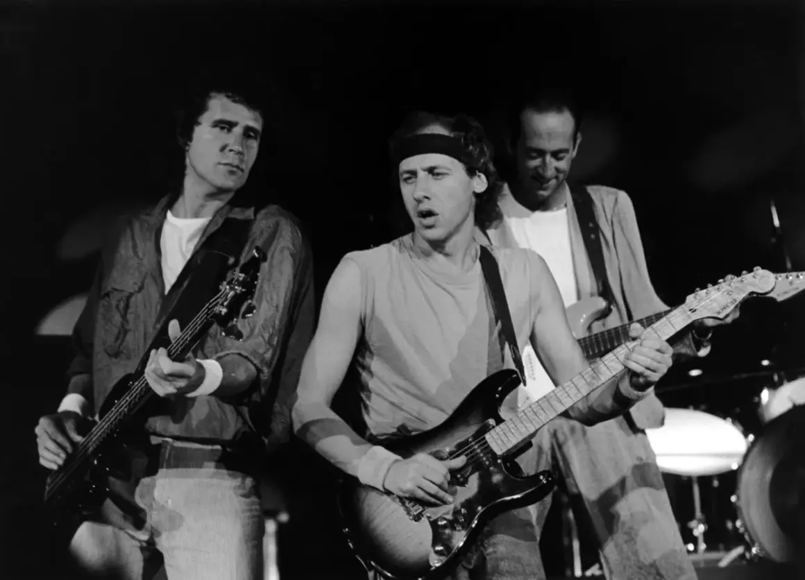 Trzech członków Dire Straits gra na gitarach podczas koncertu.