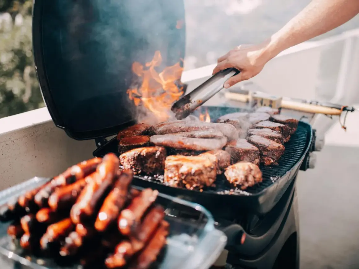 Leckeres Grillen auf dem Balkon: Würstchen und Steaks brutzeln auf dem Rost, Flammen lodern.