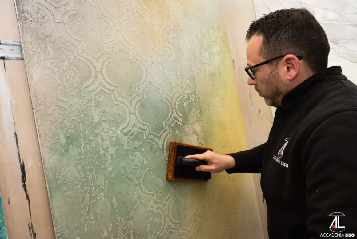 Un artigiano applica pittura per marmo su una parete con un motivo a rombi, creando un effetto materico e anticato.