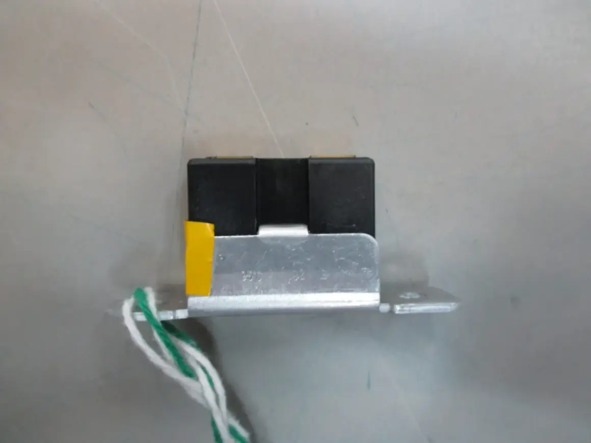 Mały, czarny element z żółtym akcentem i przewodami, przypominający wtyczkę RGB, zamontowany na metalowej płytce.