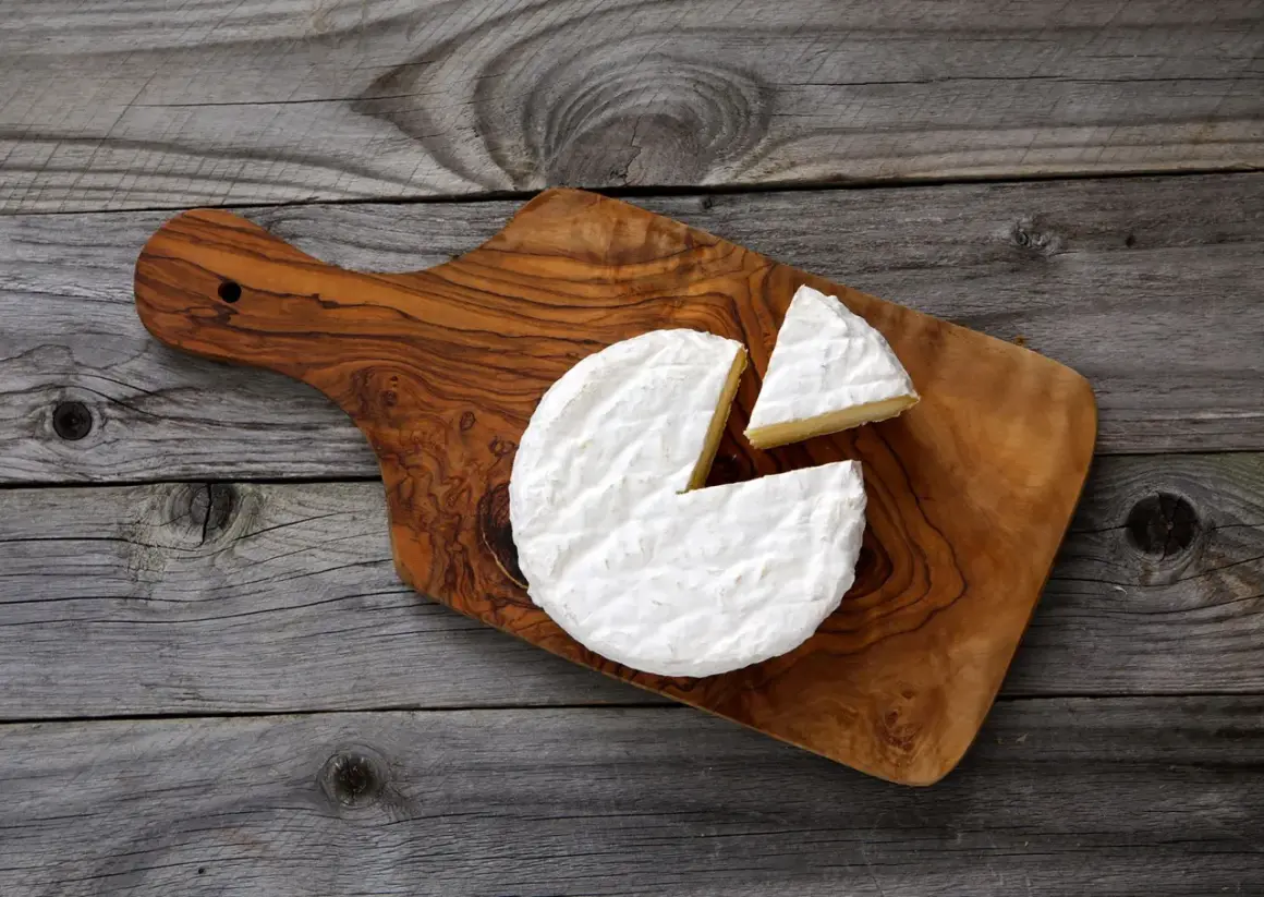 Un morceau de **brie** crémeux, avec une part coupée, sur une planche en bois rustique.