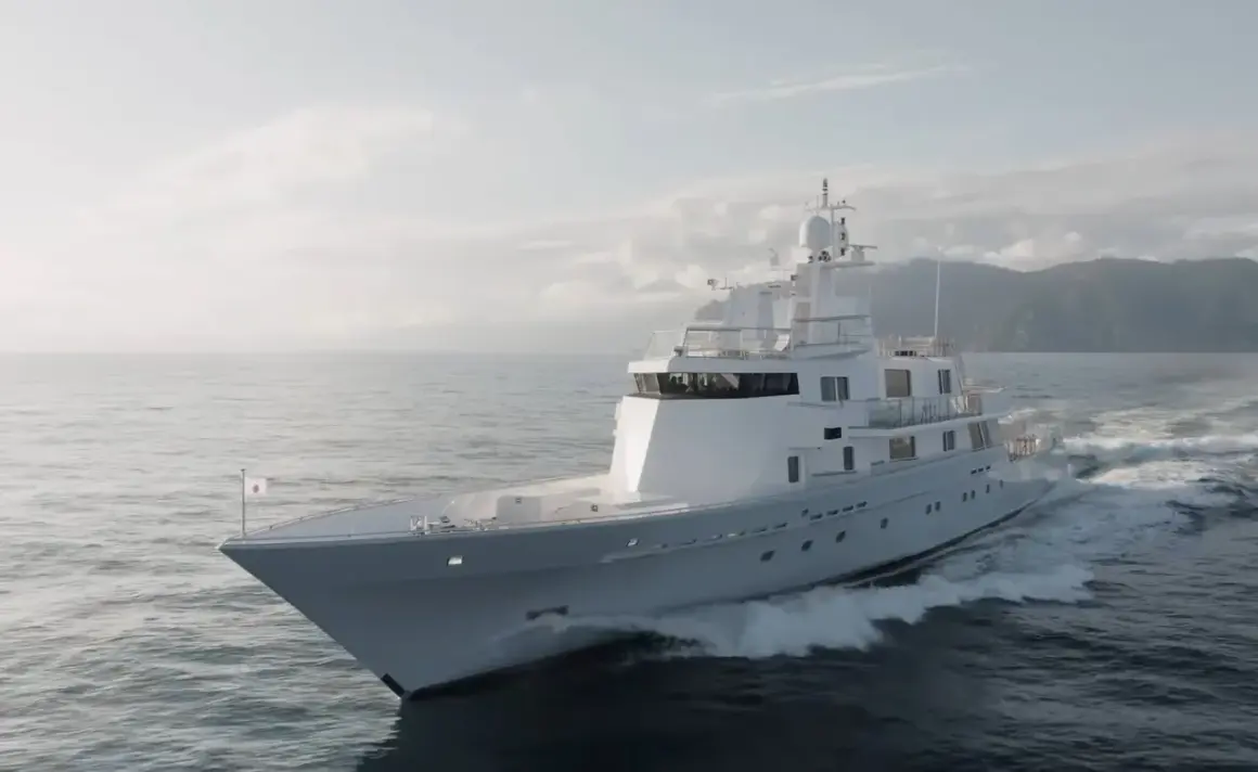 L'alessandro del bono yacht solca le onde con eleganza, un gioiello bianco su un mare calmo, con montagne sullo sfondo.
