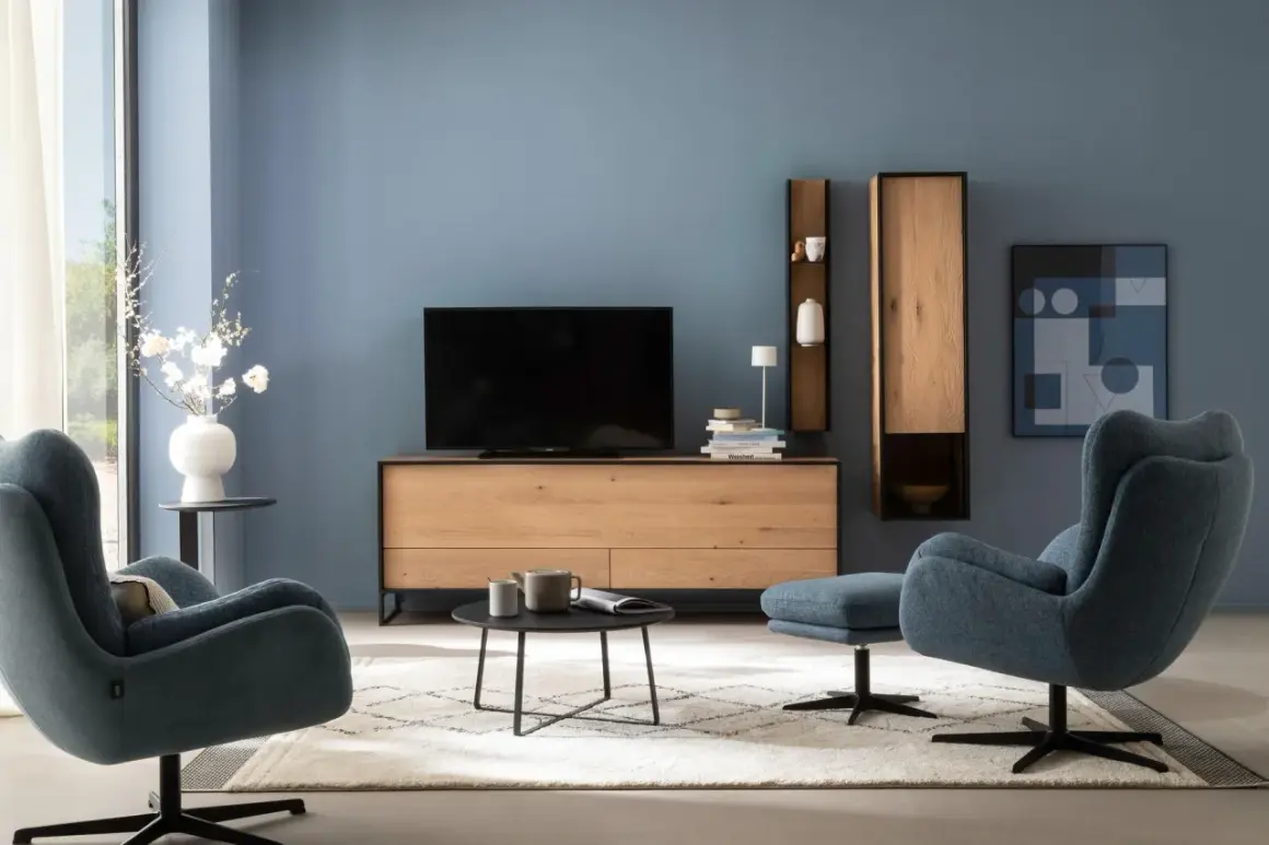 Blau passt wunderbar zu Schwarz. Ein modernes Wohnzimmer mit blauen Sesseln, einem Holzbett und schwarzem Couchtisch.