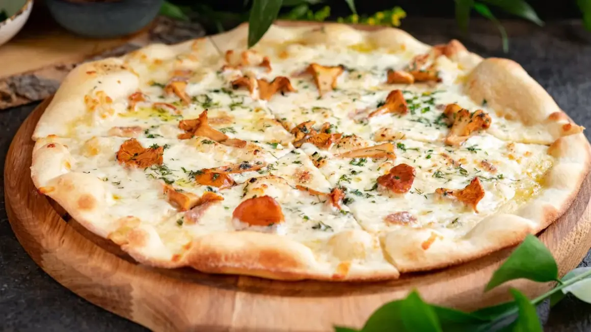 Pyszna pizza z kurkami, rozpływającym się serem i ziołami, podana na drewnianej desce.