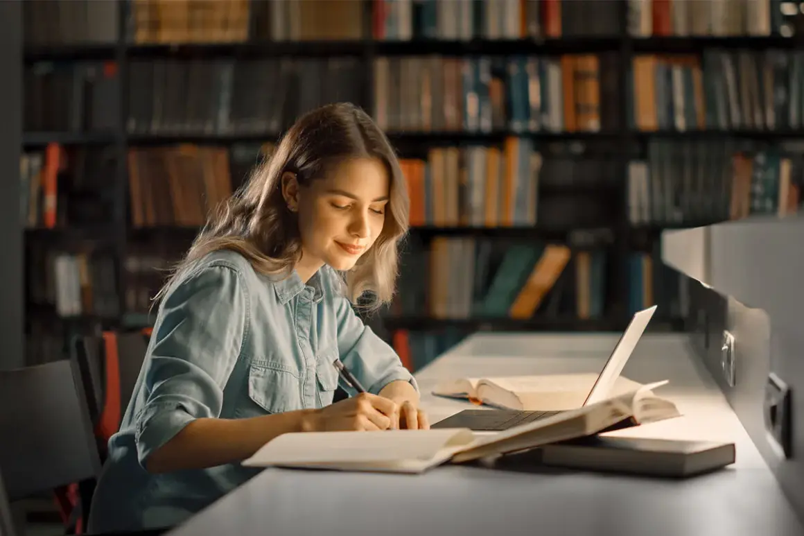 Młoda kobieta w bibliotece pisze notatki, inspirując się książkami motywacyjnymi top 10.