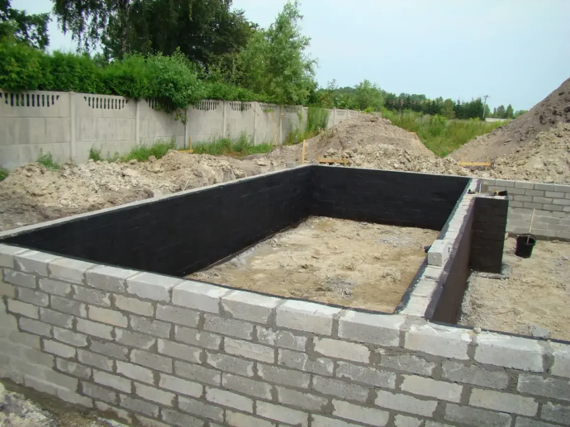 Fundament z bloczków betonowych, wewnątrz czarna izolacja. Widać kilka warstw bloczka fundamentowego.