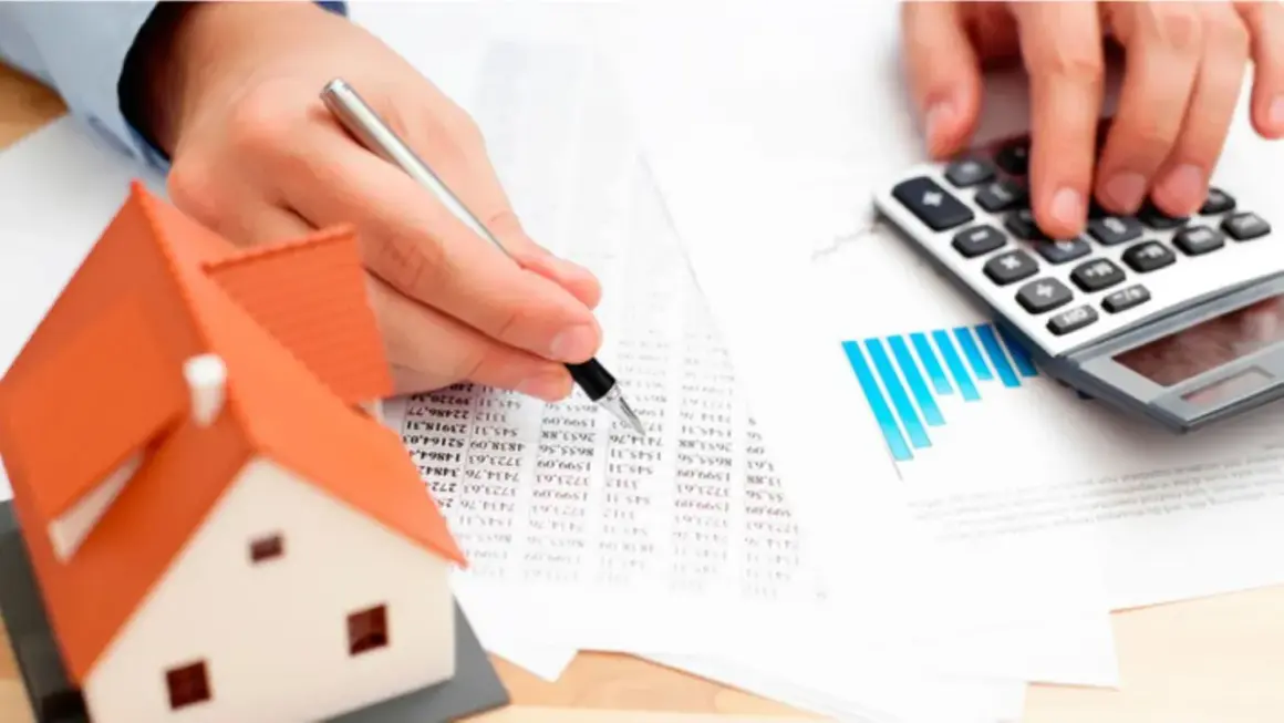 Man calculando el precio tasación vivienda con calculadora y modelo de casa.