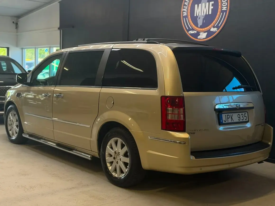En gyllene Chrysler Voyager står parkerad. Den har en takbox och en svensk registreringsskylt.