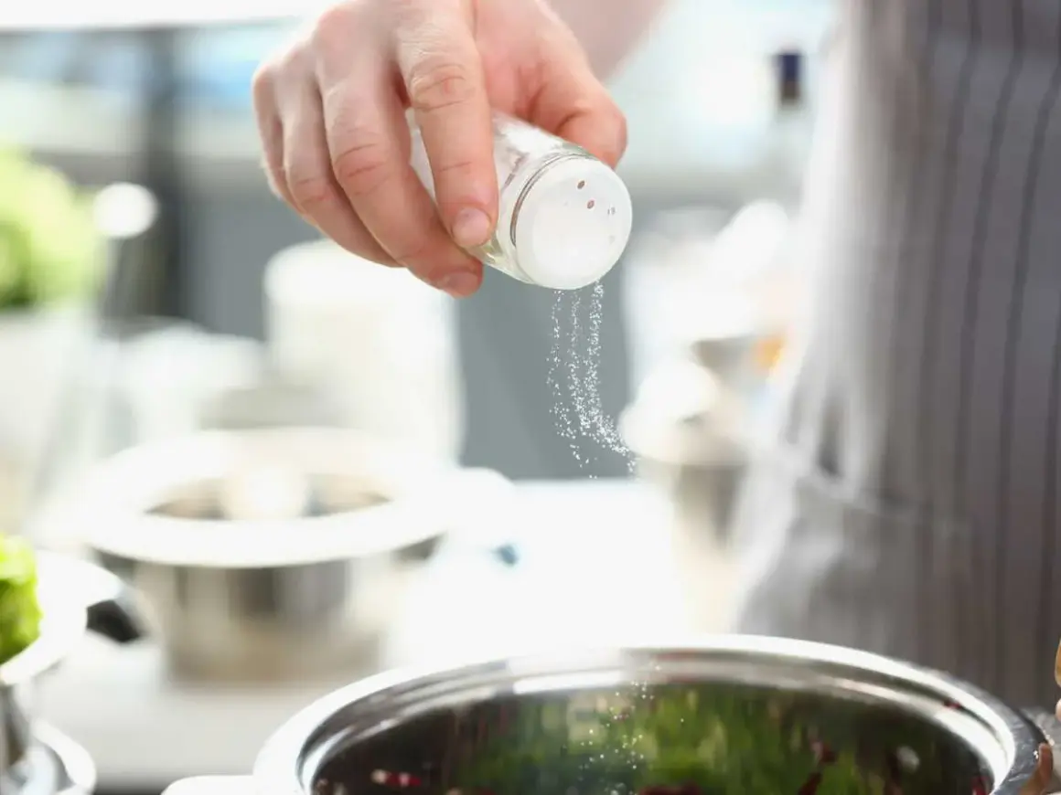 Une main saupoudre du sel dans un bol, ajoutant une touche de saveur à la cuisine.