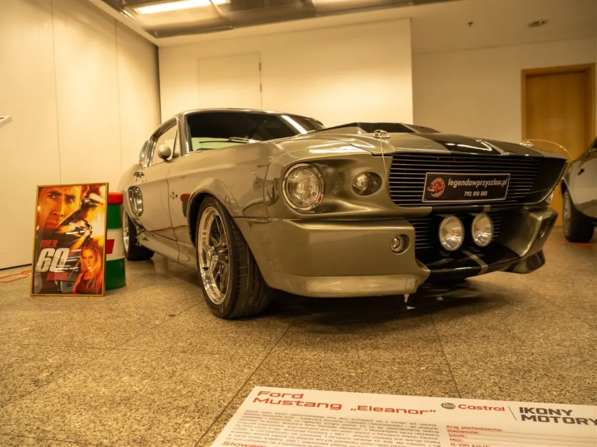 Szary Ford Mustang „Eleanor” z filmu „60 sekund” obok plakatu z Nicolasem Cage'em.