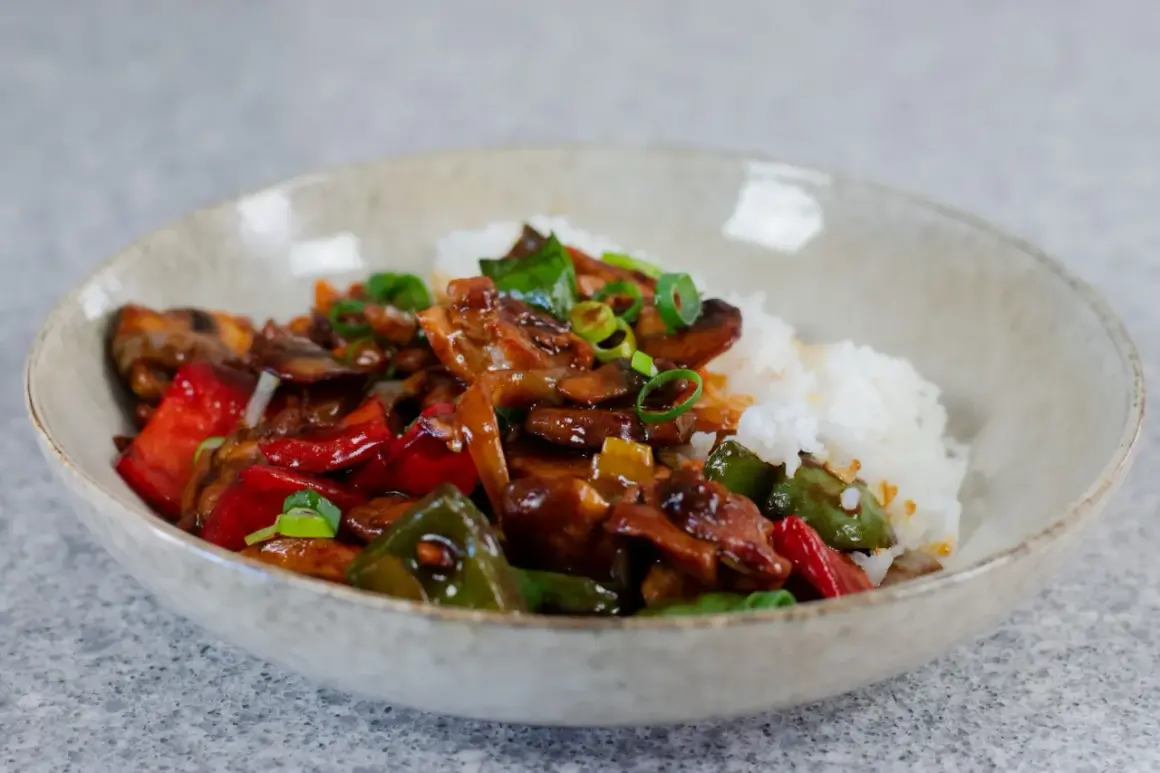 En skål med ris och en smakrik kyckling cashew-rätt med paprika och svamp, toppad med salladslök.