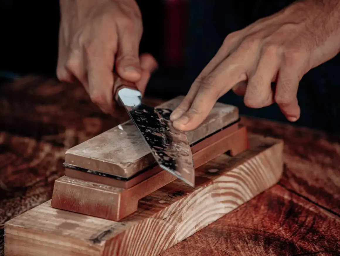 Manos afilando un cuchillo con una piedra de afilar. Aprende como afilar cuchillos con afilador para un corte perfecto.