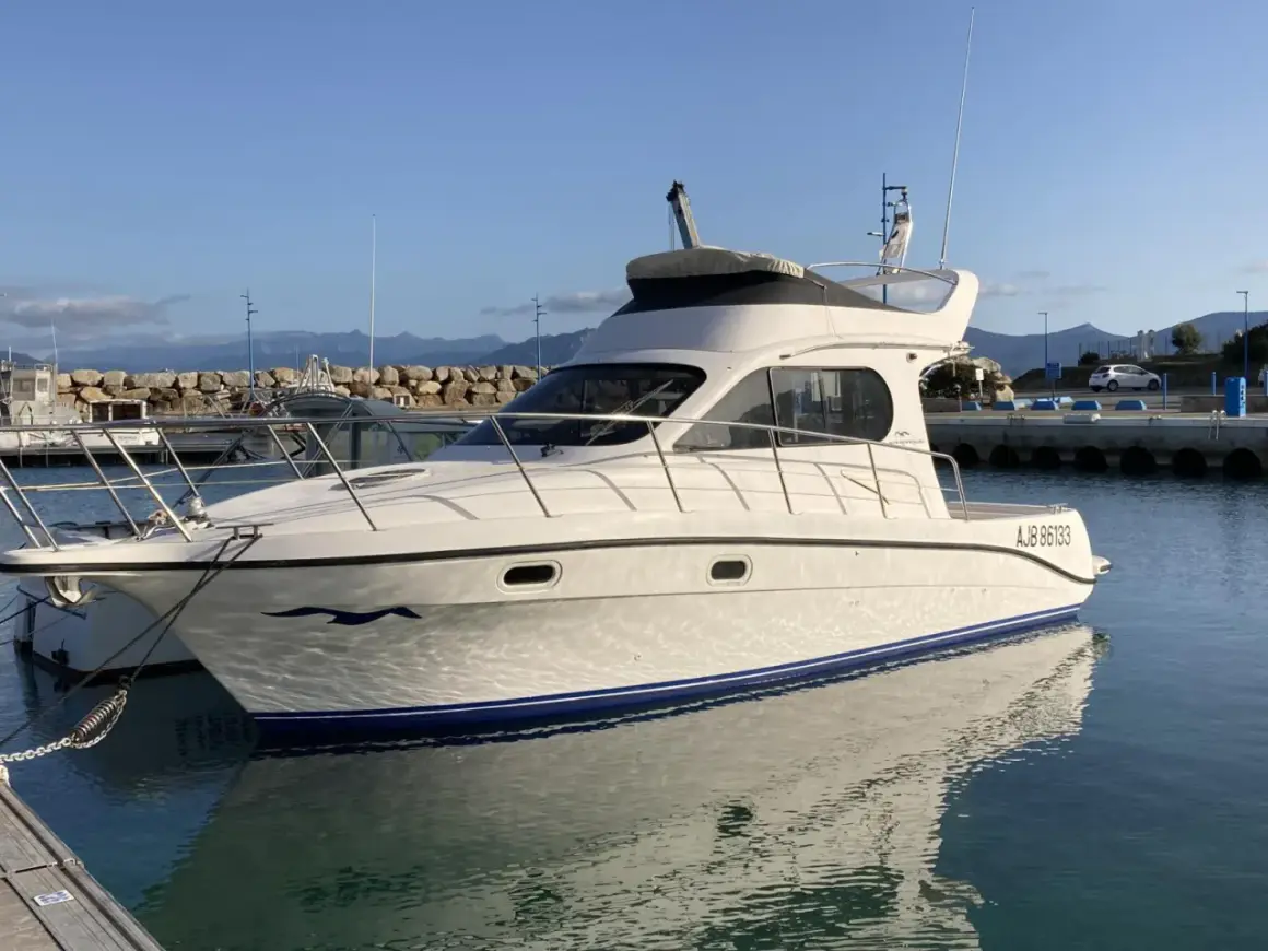 Yacht Intermare 30 ormeggiato in porto, con riflessi sull'acqua calma. Montagne sullo sfondo.