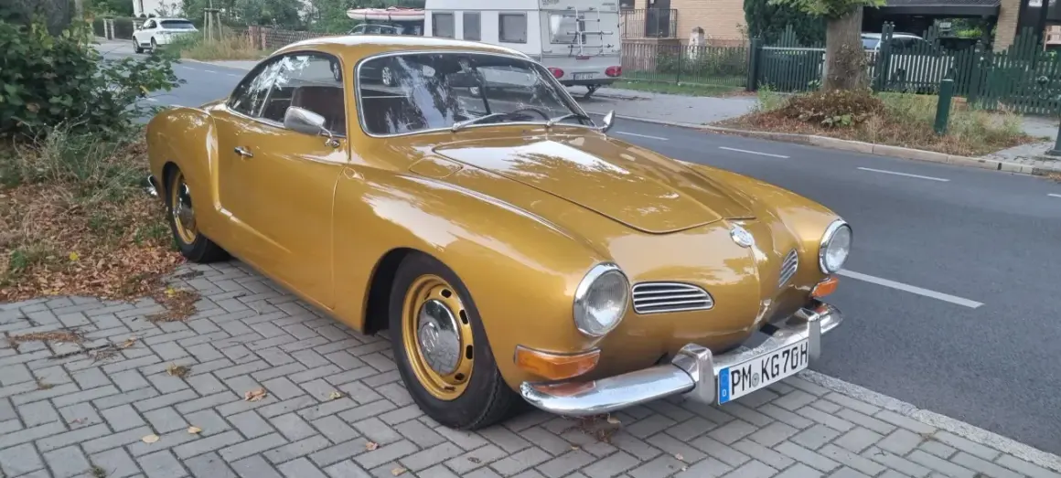 Złoty Volkswagen Karmann Ghia zaparkowany na chodniku z kostki brukowej.