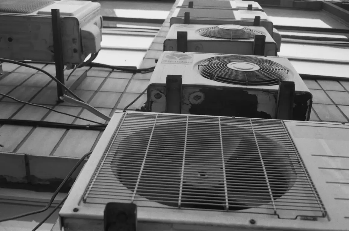 Vue en contre-plongée de plusieurs unités de climatisation extérieures, dont une pompe à chaleur triphasé, alignées sur un mur.
