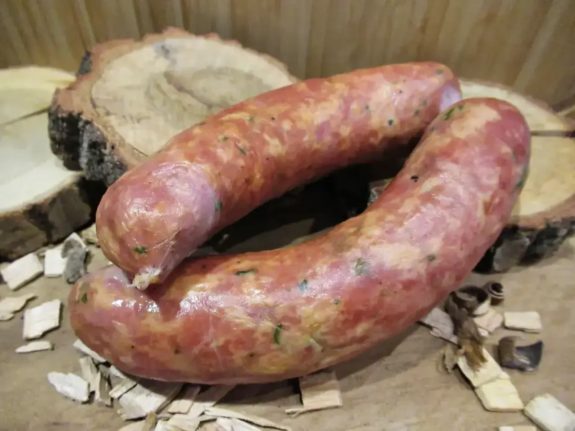 Dwie świeże kiełbasy, idealnie doprawione majerankiem, leżą na drewnianych plastrach.