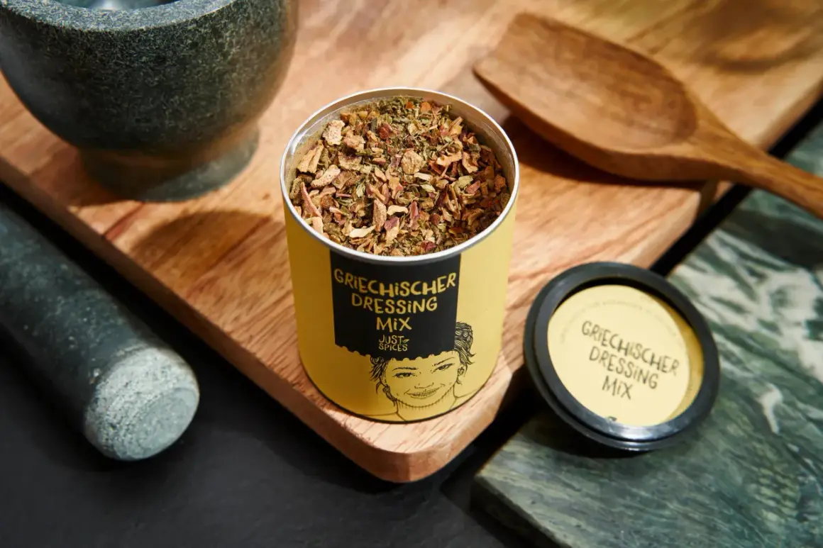 Dose mit Gewürzmischung für original griechischer salat dressing, daneben Mörser und Holzschale.