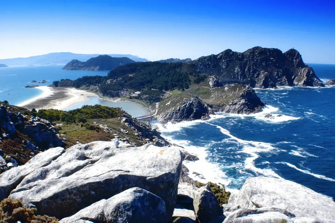 Paisaje costero con rocas, mar azul y una playa de arena blanca. Así es donde está Galicia, un paraíso natural.